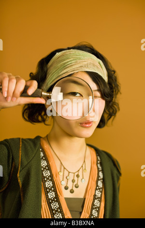 Asian woman looking through magnifying glass Banque D'Images