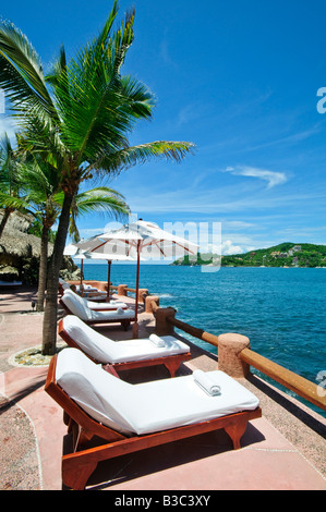 La Casa que Canta Resort Zihuatanejo Mexique | ZIHUATANEJO, Mexique — des rangées de chaises longues avec des serviettes roulées bordent une terrasse au sommet d'une falaise à la Casa que Canta, surplombant les eaux bleues profondes de la baie de Zihuatanejo sur la côte Pacifique du Mexique. Les terrasses ombragées de palmiers du complexe sont construites directement dans le promontoire de granit qui sépare la baie de l'océan. Banque D'Images