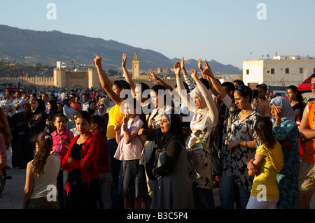 Maroc, Fes. Sur la toile de fond des anciens remparts et mosquées de la médina du 13e siècle, les jeunes non-voilée et voilée de femmes marocaines profitez d'un concert gratuit à la place Boujloud pendant le Festival de Fès des Musiques Sacrées du Monde. Banque D'Images