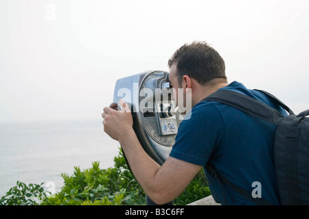 Un jeune homme regarde à travers des jumelles à monnayeur à la mer Banque D'Images