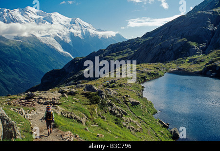 France, Haute-Savoie, Chamonix. Un Walker dirige le long du sentier par un tarn sur le Tour de Pays du Mont Blanc face au Mont Blanc au-dessus de Chamonix. Banque D'Images