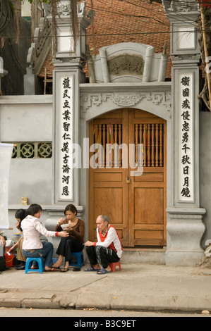 Un groupe de Vietnamiens s'assoient sur de petites chaises en plastique dans un restaurant de fortune situé dans la rue à l'extérieur d'un temple chinois à Hanoi Vietnam Banque D'Images