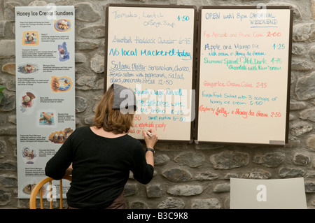 Femme écrivant l'alimentation quotidienne de repas promotions sur menu écrit à bord de la Ruche sur le quai restaurant Aberaeron Wales UK Banque D'Images