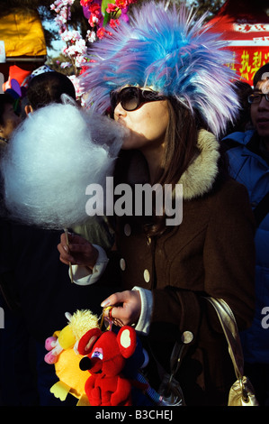 La Chine, Beijing. Fête du Printemps le Nouvel An chinois - le Parc Ditan foire du temple. Une fille de manger de la barbe à papa et de porter un costume hat. Banque D'Images