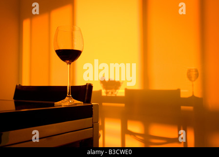 Verre de vin rouge sur une table au coucher du soleil avec orange ombres projetées sur un mur Banque D'Images