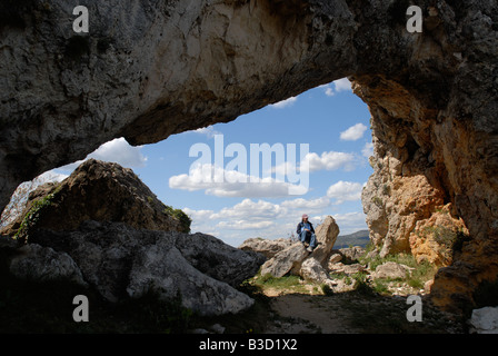 Randonneur femme assise sous Forada Rock Arch, Sierra de la Forada, Province d'Alicante, Communauté Valencienne, Espagne Banque D'Images