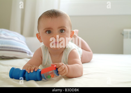 Un bébé s'allonge sur le lit des parents tout en jouant avec un jouet Banque D'Images