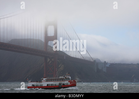 Un bateau d'excursion de la baie de San Francisco, l'Harbour Queen, passe par l'extrémité nord du pont du Golden Gate, qui est enveloppé dans le brouillard. Banque D'Images