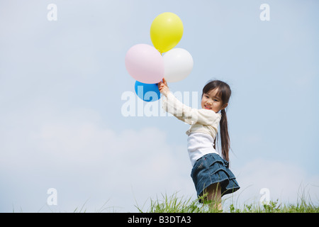 Girl holding colorful balloons against blue sky Banque D'Images