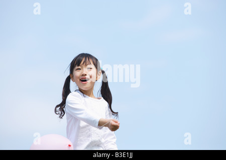 Smiling girl Playing with balloon against blue sky Banque D'Images