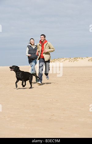 Couple running on beach with dog Banque D'Images