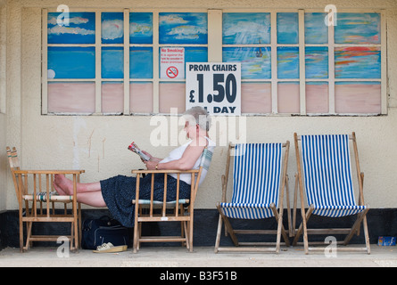 Pensionné senior woman reading newspaper assis dans une chaise longue Banque D'Images