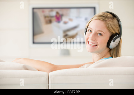Femme dans le salon à regarder la télévision et portant des écouteurs smiling Banque D'Images