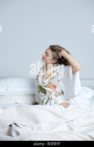 Jeune femme en robe de chambre s'étend au lit Banque D'Images