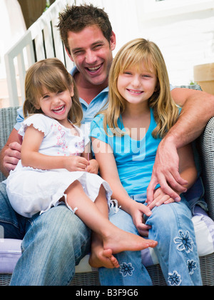 Homme et deux jeunes filles assis sur patio smiling Banque D'Images