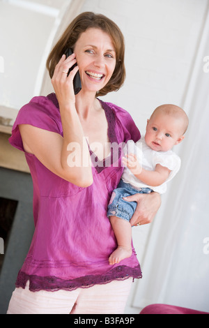 Mère dans la salle de séjour à l'aide téléphone holding baby smiling Banque D'Images