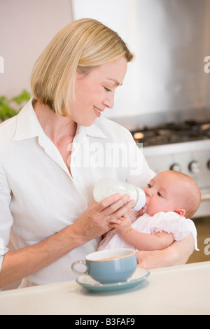 Mère de nourrir bébé dans la cuisine avec cafetière smiling Banque D'Images