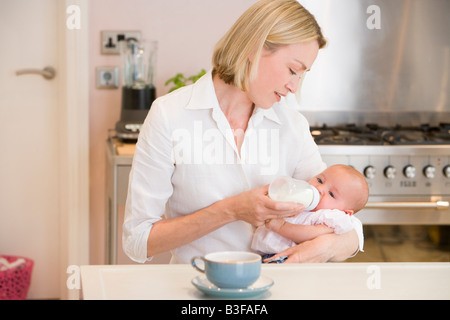 Mère de nourrir bébé dans la cuisine avec cafetière Banque D'Images