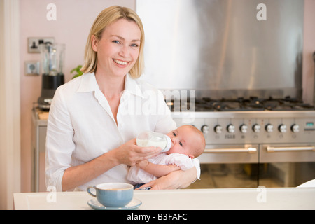 Mère de nourrir bébé dans la cuisine avec cafetière smiling Banque D'Images