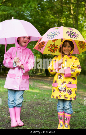 Deux soeurs à l'extérieur dans la pluie avec parasols smiling Banque D'Images