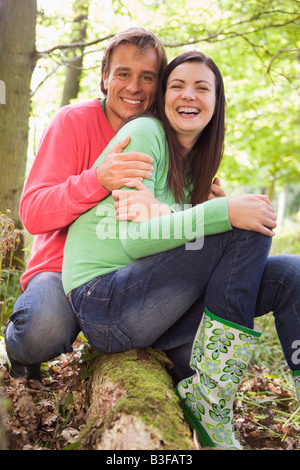 Couple outdoors in woods assis sur log smiling Banque D'Images