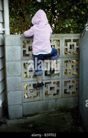 Sur le mur, petite fille de cinq ans se hisse dessus sur un mur du jardin bas Banque D'Images