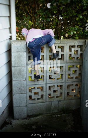 Sur le mur, petite fille de cinq ans se hisse dessus sur un mur du jardin bas Banque D'Images