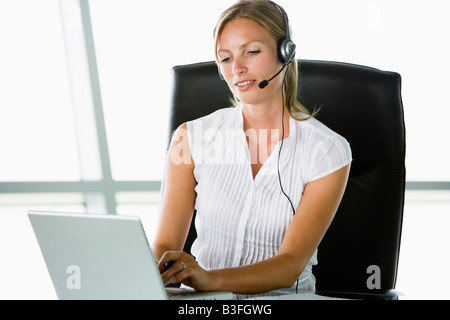 Businesswoman sitting in office wearing headset using laptop Banque D'Images