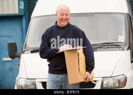 Deliveryperson standing avec van avec presse-papiers et fort smiling Banque D'Images