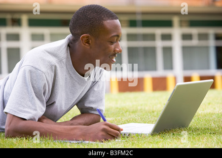 Student lying outdoors sur pelouse avec coffre Banque D'Images