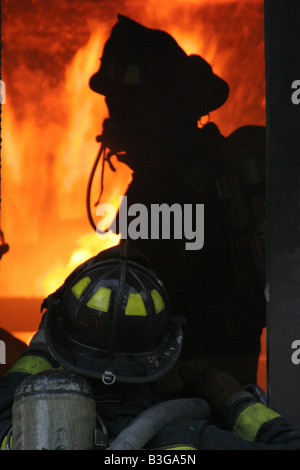 Trois pompiers à la recherche d'une pièce d'une maison en feu avant d'éteindre les flammes Banque D'Images