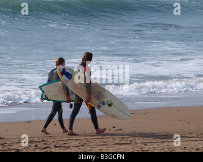 Deux surfeurs de marcher le long de la plage en début de soirée. Cornwall, UK Banque D'Images