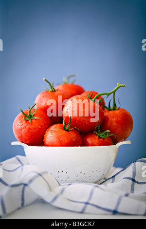 Les tomates avec des tiges dans une passoire blanche sur un fond bleu Banque D'Images