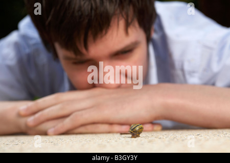 jeune adulte mâle adolescent regardant un escargot se déplaçant lentement le long d'un patio de jardin Banque D'Images