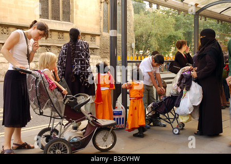 Les mères et leurs enfants sont debout ensemble en attendant à un arrêt de bus public dans une rue d'Oxford, Oxfordshire, Angleterre. Banque D'Images