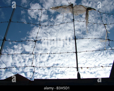 Fil de fer barbelé de sécurité le long du toit de protection locaux silhouetté contre le ciel bleu avec des nuages blancs Banque D'Images