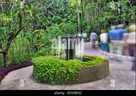 Une longue exposition de personnes passant devant une fontaine d'eau qui coule dans les jardins botaniques de Singapour. Banque D'Images