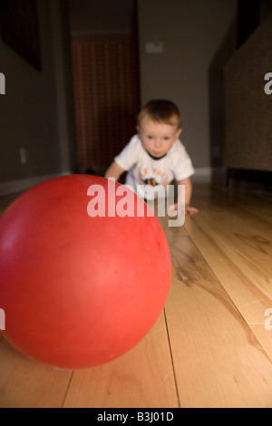 Huit mois bébé garçon ramper vers ballon rouge à la maison Banque D'Images