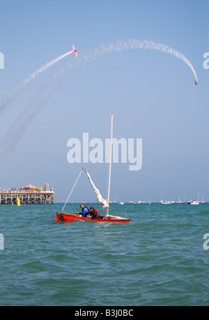 Un couple dans un bateau à voile au large de la plage de Bournemouth, Bournemouth durant la fête de l'air. Biplan afficher sur la jetée. Le Dorset. Banque D'Images