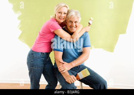 Portrait of smiling couple assis en face de la moitié mur peint avec les pinceaux Banque D'Images