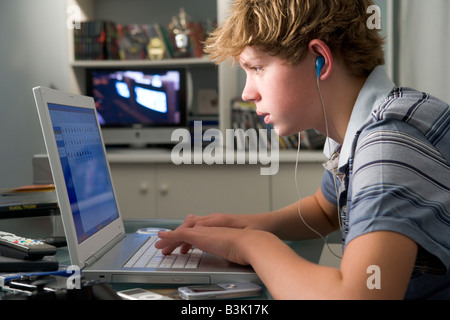 Jeune garçon dans la chambre à l'aide d'ordinateur portable et listening to MP3 player Banque D'Images