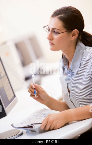 Woman in computer room entourant les éléments dans un journal Banque D'Images