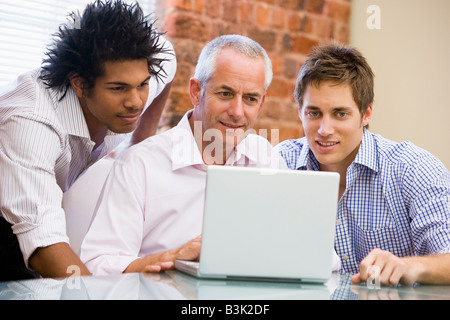 Trois hommes d'dans office looking at laptop smiling Banque D'Images