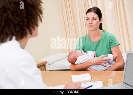 Médecin avec ordinateur portable et la femme dans le cabinet du médecin holding baby Banque D'Images