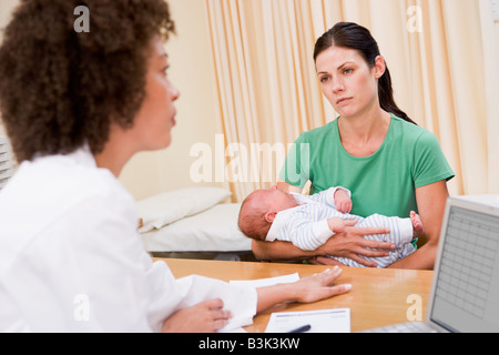 Médecin avec ordinateur portable et la femme dans le cabinet du médecin holding baby Banque D'Images