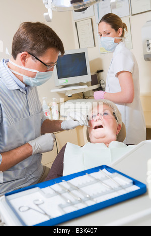 Dentiste et assistant en salle d'examen avec femme en fauteuil Banque D'Images