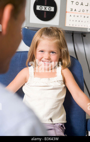 Optométriste dans la salle d'examen avec jeune fille en chaise smiling Banque D'Images