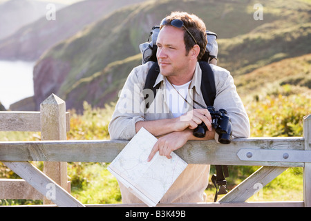 Man relaxing on cliffside path holding map et jumelles Banque D'Images