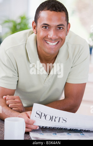 Man in kitchen reading newspaper and smiling Banque D'Images