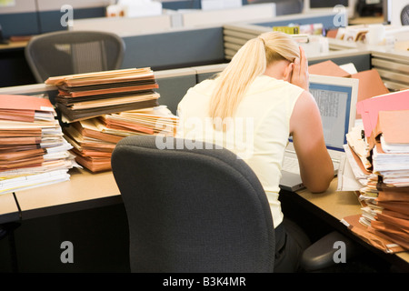 Businesswoman in cubicle avec ordinateur portable et les piles de dossiers Banque D'Images